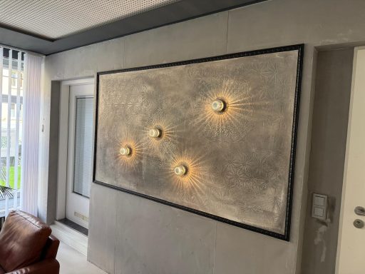 Wandkunst mit vier runden Leuchten auf einer strukturierten grauen Fläche.