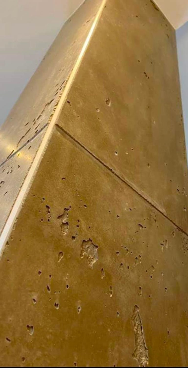 Echtmetall Mikrozement Ein gehobelter Betonpfeiler mit glatter goldener Oberfläche in Innenraum.