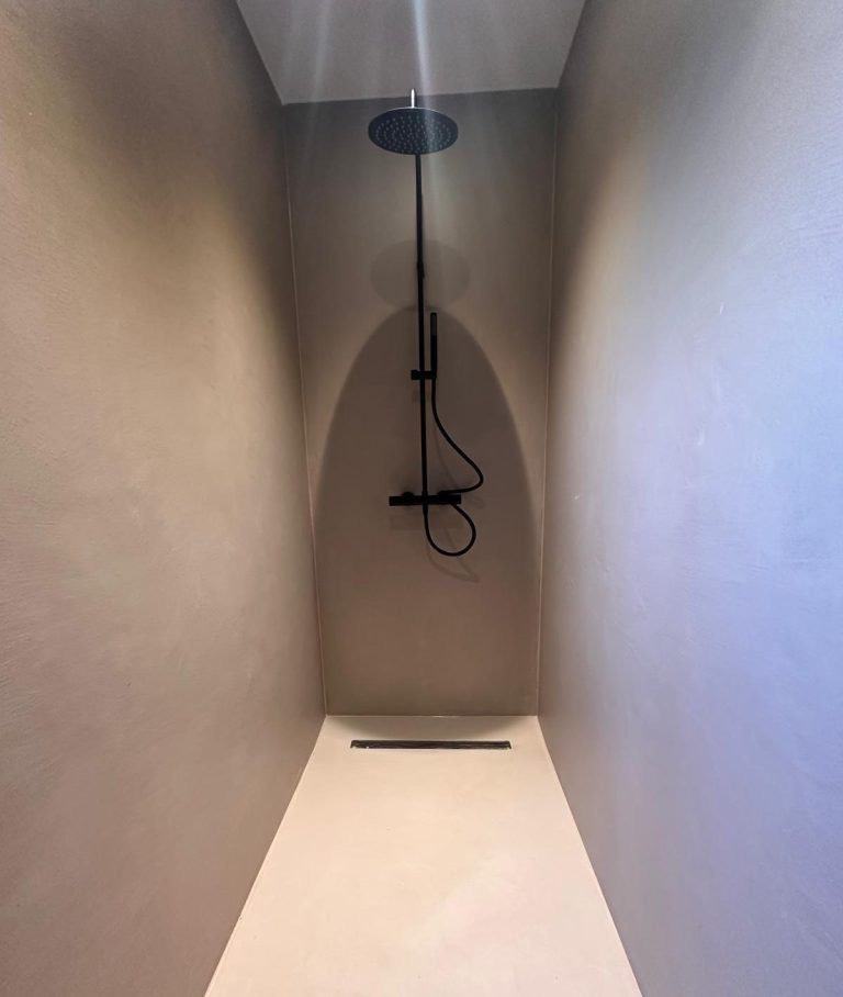 Mikrozement Bad Minimalist Duschbereich mit einer schwarzen Badezimmerarmatur und gefliesten Wänden.