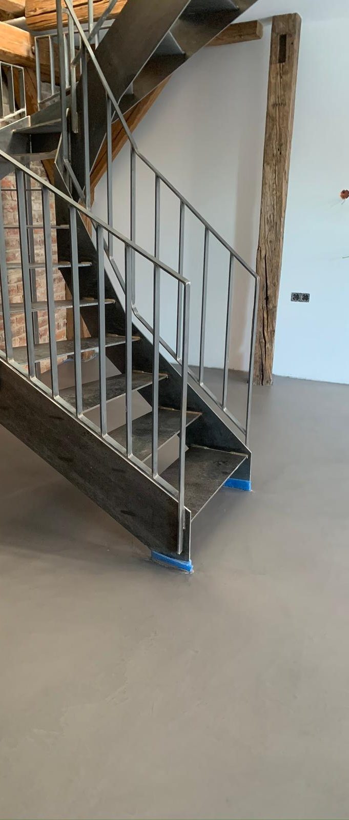 Treppenhaus mit schwarzer Treppe und metallischem Geländer, auf einem grauen Mikrozement Boden.