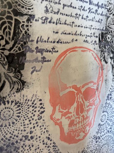 Muster mit einer Schädelgrafik und handschriftlichem Text auf hellem Hintergrund.