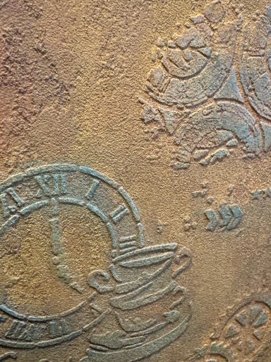 Strukturierte Oberfläche mit Uhren und dekorativen Mustern in Bronze- und Erdtönen.