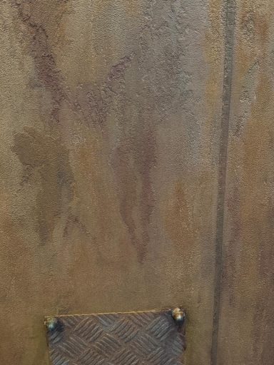 Texturierte Wand mit braunen und rostfarbenen Mustern, darunter ein gewebter Korb.